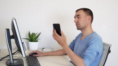 Yetişkin adam iş yerinde akıllı telefondan konuşuyor. Beyaz adam akıllı telefondan bir şeyler konuşuyor. Evde çalışan yakışıklı biri..