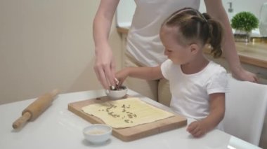 Sevimli bebek kız ve anne puf böreğinin üzerine ayçekirdeği serperler. Annesiyle küçük tatlı bir kız mutfakta yemek pişiriyor..