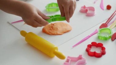 Küçük tatlı kız plasticinle oynuyor. Masanın üzerindeki görüntüyü plastik ve oyuncaklarla kapat.