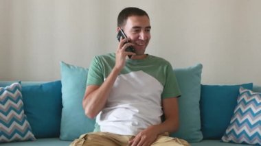 Yakışıklı genç adam çağrıya cevap verir ve akıllı telefondan konuşur. Gülümseyen adam evdeki kanepede oturur ve akıllı telefondan sesli arama yapar..