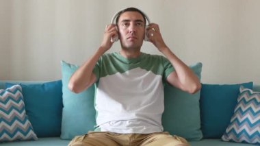 Yakışıklı genç adam kablosuz kulaklık takıyor ve müzik dinliyor. Rahat adam evdeki kanepede oturur ve kablosuz kulaklıkla müzik dinler..