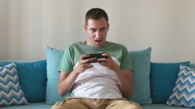 Genç adam akıllı telefondan oynar ve kazanır. Konsantre adam akıllı telefonuyla oynar ve evinde kanepede otururken kazanmanın sevincini yaşar..