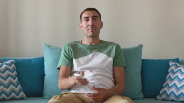 Mutlu genç adam komik TV dizileri ya da videolar izler ve güler. Yakışıklı adam kanepede otururken televizyon izler ve gülümser..