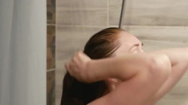 Güzel bir kadın banyoda saçlarını ıslatıyor. Genç kızıl saçlı kadın banyoda saç yıkıyor..