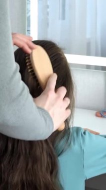 Anne aynanın önünde küçük kızının saçını tarıyor. 7 yaşındaki bir kızın uzun saçlarının örüldüğü yakın plan. Anne-kız randevusu kavramı.