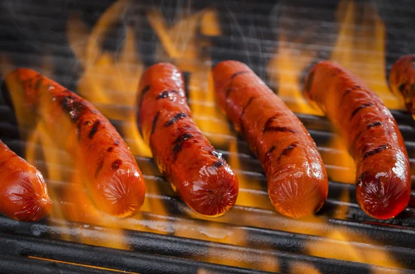 Deliziosi hot dog che cucinano su una griglia fiammeggiante calda — Foto Stock