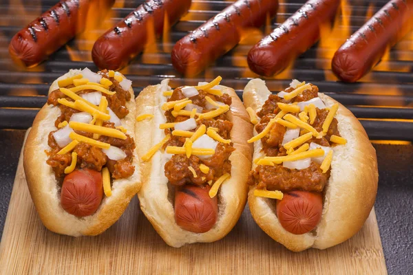 Tre hot dog chili e barbecue fiammeggiante Sfondo griglia — Foto Stock