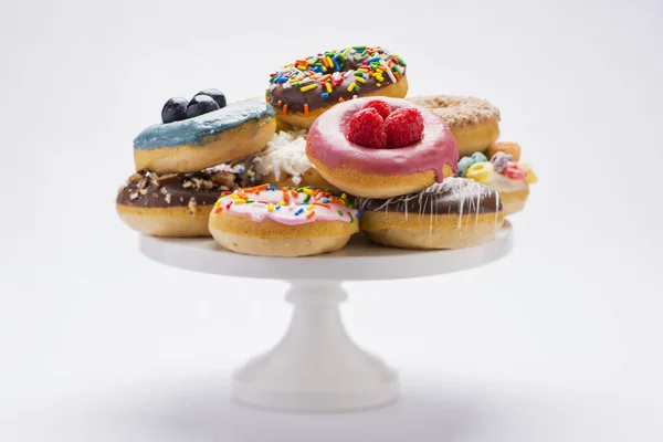 Een verscheidenheid van kleurrijke verse donuts op een witte voetstuk geïsoleerd op wit Stockfoto
