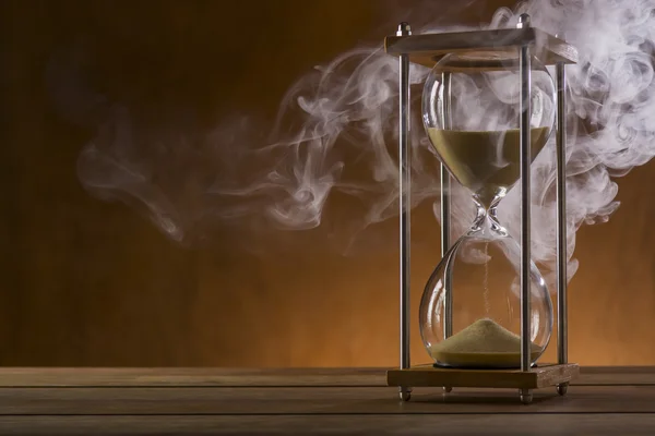 Reloj de arena con humo sobre un fondo rústico Imagen de archivo