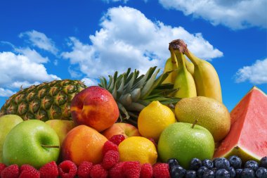 Assortment of exotic fruits and blue sky with puffy white clouds clipart