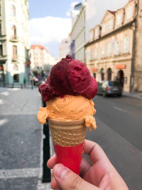 Elinde pembe ve turuncu kıvrımlı dondurma külahı tutan biri. Koni kırmızı ve beyaz.