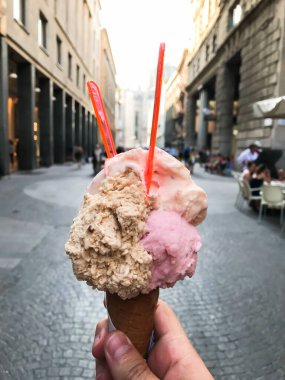 Elinde pembe ve turuncu kıvrımlı dondurma külahı tutan biri. Koni kırmızı ve beyaz.