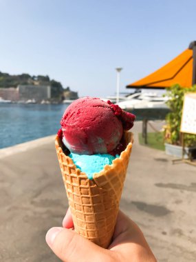 Elinde pembe ve mavi kıvrımlı dondurma külahı tutan biri. Koni