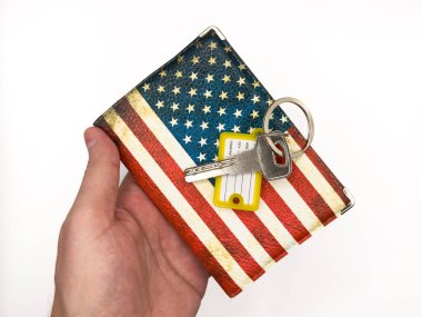 Keys, door kyes, home keys, mortgage in the USA, apartment for rent in the US, housing, buying a house in the USA, apartment mortgage, house rental loan. US flag, dollars. A hand holding a key with yellow keychain