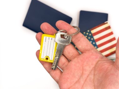 Keys, door kyes, home keys, mortgage in the USA, apartment for rent in the US, housing, buying a house in the USA, apartment mortgage, house rental loan. US flag, dollars. A hand holding a key with yellow keychain