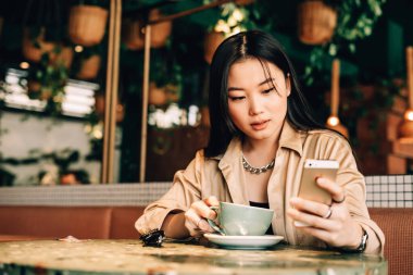 Asyalı kız telefonda konuşuyor ve kafede kahve içiyor.