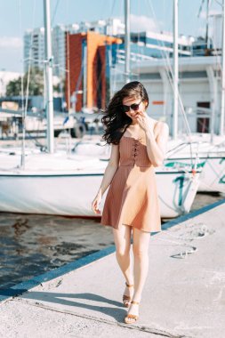 Genç, güzel, sağlıklı bir kadın rıhtımın arka planında, rıhtımda yürüyor. Yazın deniz limanı. Hafta sonu gezisi.