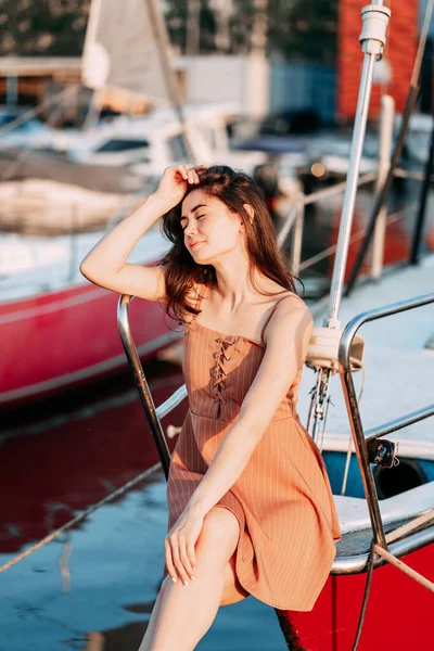 Elbiseli genç bir kız, yaz akşamları bir iskelede bir teknede oturur. Batan güneş, tatil.