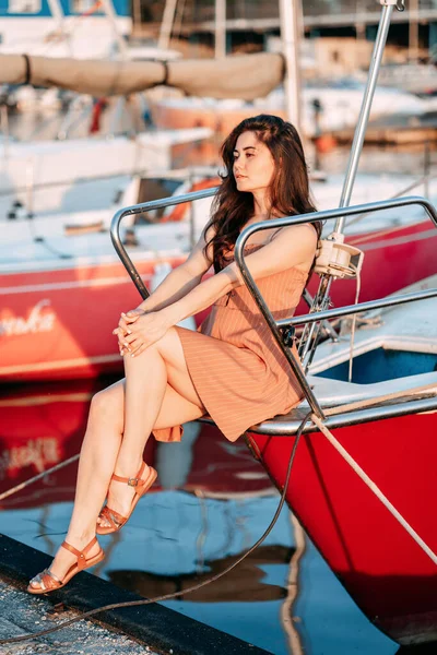 Elbiseli genç bir kız, yaz akşamları bir iskelede bir teknede oturur. Batan güneş, tatil.
