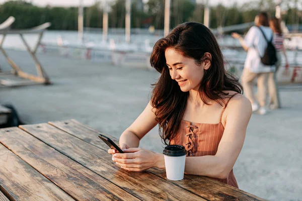 Genç kız bir masada oturuyor, dışarıda kahveli bir telefon kullanıyor. Yat kulübü, deniz, deniz tatili. Genç bir kız telefonuna mesaj yazıyor, Summer.