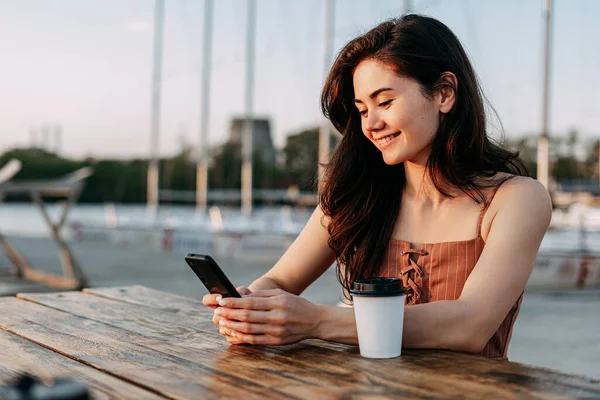 Genç kız bir masada oturuyor, dışarıda kahveli bir telefon kullanıyor. Yat kulübü, deniz, deniz tatili. Genç bir kız telefonuna mesaj yazıyor, Summer.