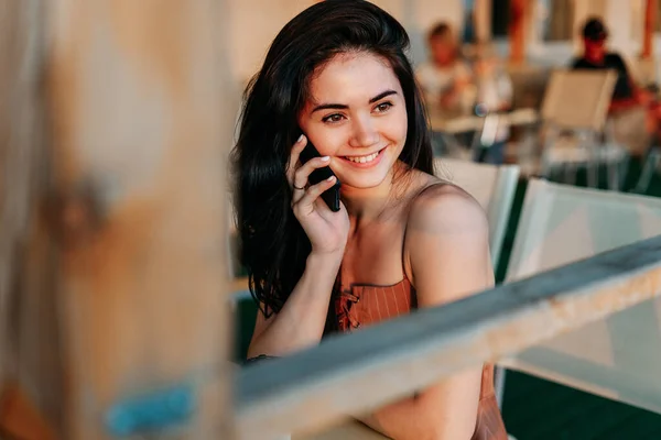 Genç, güzel, mutlu esmer kız telefonda konuşuyor, gülüyor, kafede..