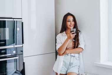 Asyalı kadın evdeki mutfakta şarap içiyor.