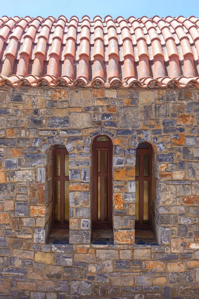 Stone building with red roof tiles and three narrow windows