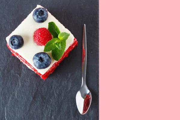 Draufsicht auf ein Stück Kuchen mit Blaubeeren und Himbeeren auf rosa Hintergrund dekoriert. roter Samtkuchen mit Beeren — Stockfoto