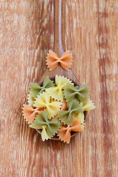 Close-up with Italian farfalle pasta in a wooden spoon on a wooden background. Colored pasta overhead shot — Stock Photo, Image