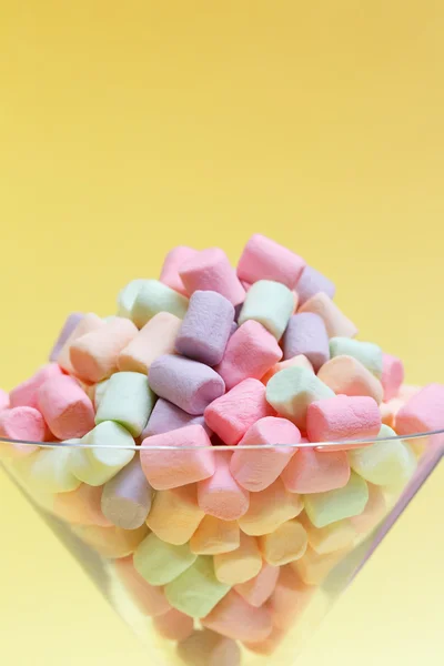 Close-up of pastel colored marshmallow in a glass goblet on a yellow background — Stock Photo, Image