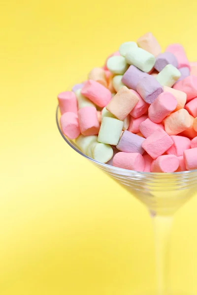 Bovenaanzicht van pastel gekleurde marshmallow in een glas goblet op een gele achtergrond. Minimalisme stijl. — Stockfoto