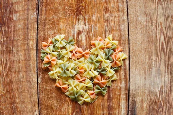 Farfalle pasta italiana en forma de corazón sobre un fondo de madera plano — Foto de Stock