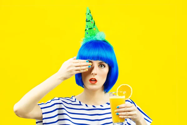Bir bardak portakal suyu sarı bir arka plan üzerinde tutan mavi bir peruk kız