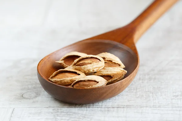 Unpeeled almonds in a wooden spoon on a light background — Stock Photo, Image