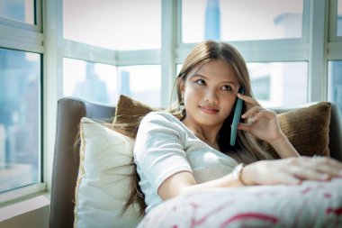 Online Flört Konsepti, kanepede akıllı telefon kullanan güzel Asyalı kız.