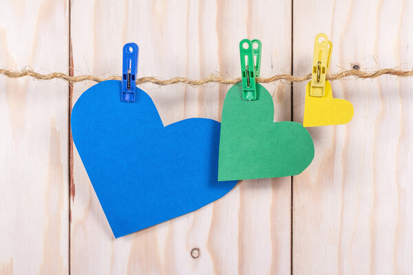 Color paper hearts on rope with clothespin on wooden background