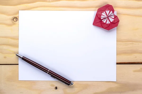 Valentijnskaart met origami rood hart en pen op houten tafel — Stockfoto