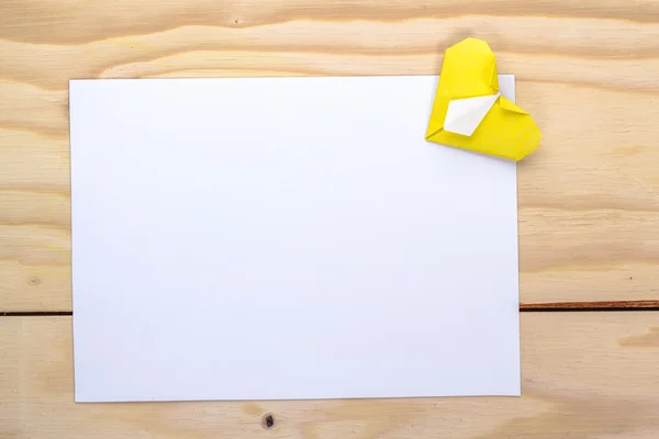 White page with origami yellow heart on wooden table