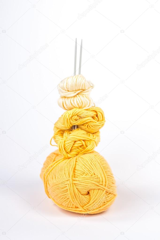 Isolated stack of several balls of yellow yarn with knitting needles