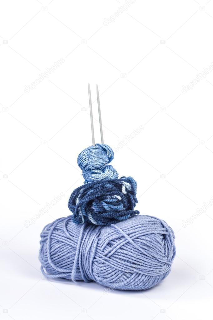 Isolated stack of several balls of blue yarn with knitting needles