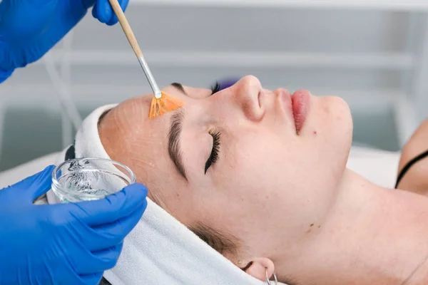 Kozmetik salonunun genç bayan müşterisi yüz temizleme ameliyatı oluyor. Doktor kozmetik uzmanı deri temizliyor. Cilt bakımı ve güzellik salonu veya klinik kavramları.