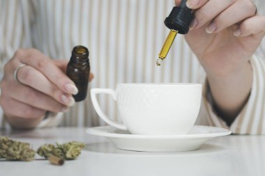 CBC yağlı pipetle kahve fincanlarına damlayan bir kadının el ele çekimi. Alternatif tıp kavramları, doğal ağrı kesici ve şifalı bitkiler.