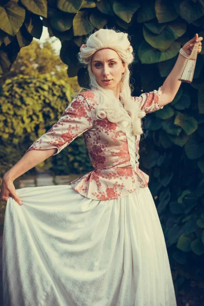 Portrait of blonde woman dressed in historical Baroque clothes with old fashion hairstyle, outdoors. Luxurious medieval dress