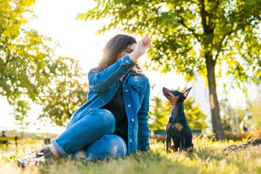 Genç bir kadın dışarıda oynayıp köpeğini eğitiyor. Siyah ve Tan minyatür. Parkta sahibi olan dişi bir köpek.