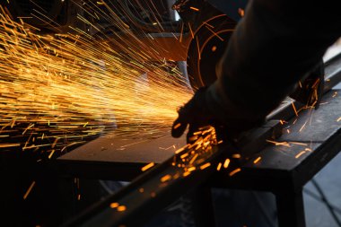 Yetişkin bir erkek eski bir atölyede çalışıyor. Elinde metal bir kesme makinesi var ve metal bir ce kesiyor. Boşluğu kopyala.