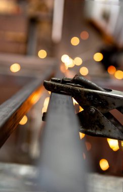 Kaynak makinesindeki penseye odaklanmış durumda. Arkasında da boruları kaynak yapan işçi var..