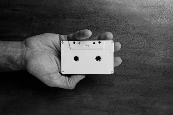 stock image There is a white audio magnetic cassette in the man's hand. Below is a wooden background. Black and white
