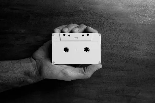 stock image There is a white audio magnetic cassette in the man's hand. Below is a wooden background.