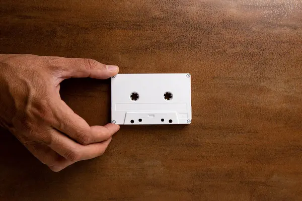 A man\'s hand grabs a white magnetic audio tape on a wooden base. Audio cassette. Music.